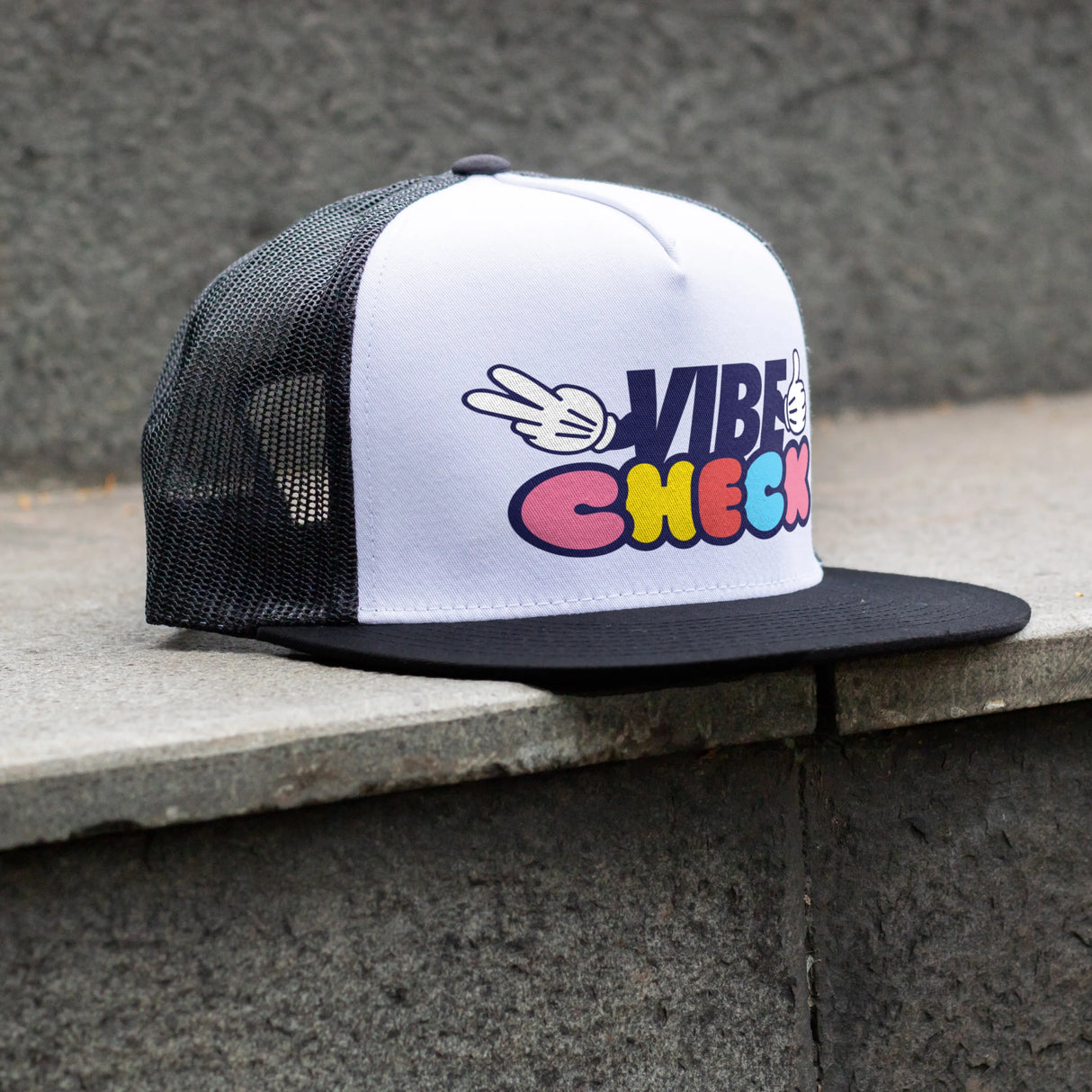 White and black cap with colorful direct to film transfer on the front sitting on a concrete surface.
