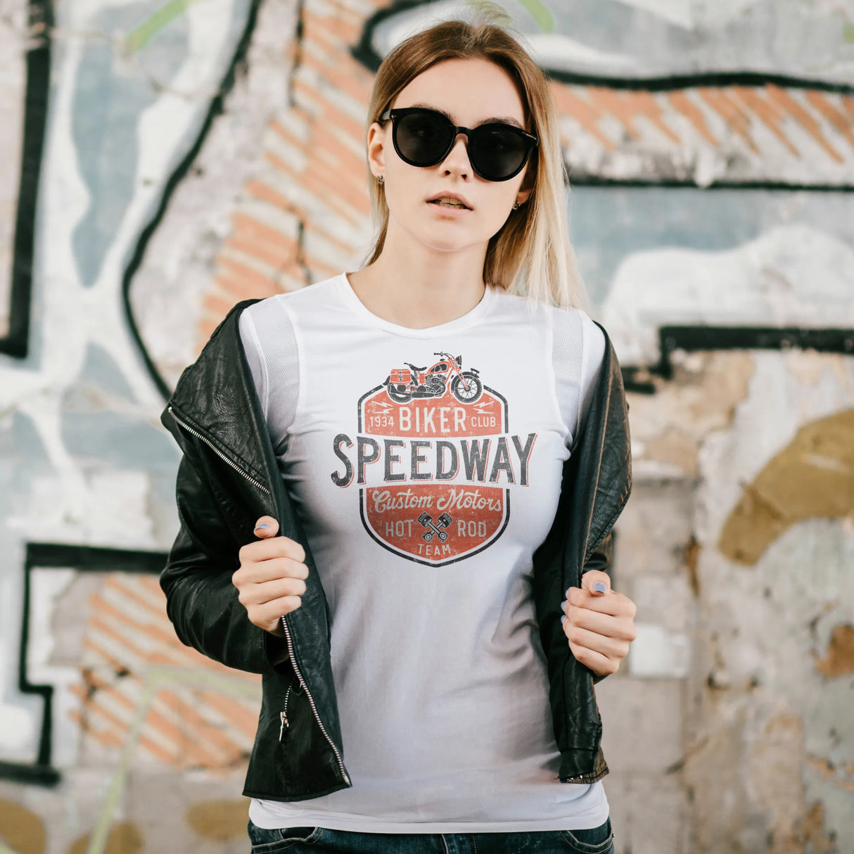 Person wearing a white t-shirt with a graphic design and text, standing in front of a graffiti-covered wall.