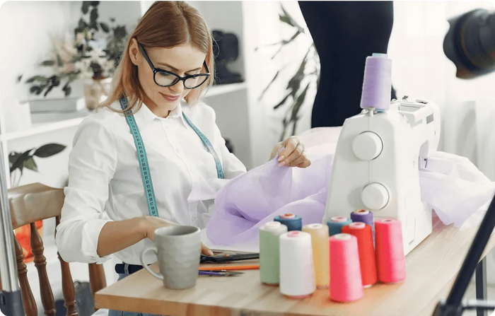 Woman working at a sewing machine with colorful spools of thread on a table.